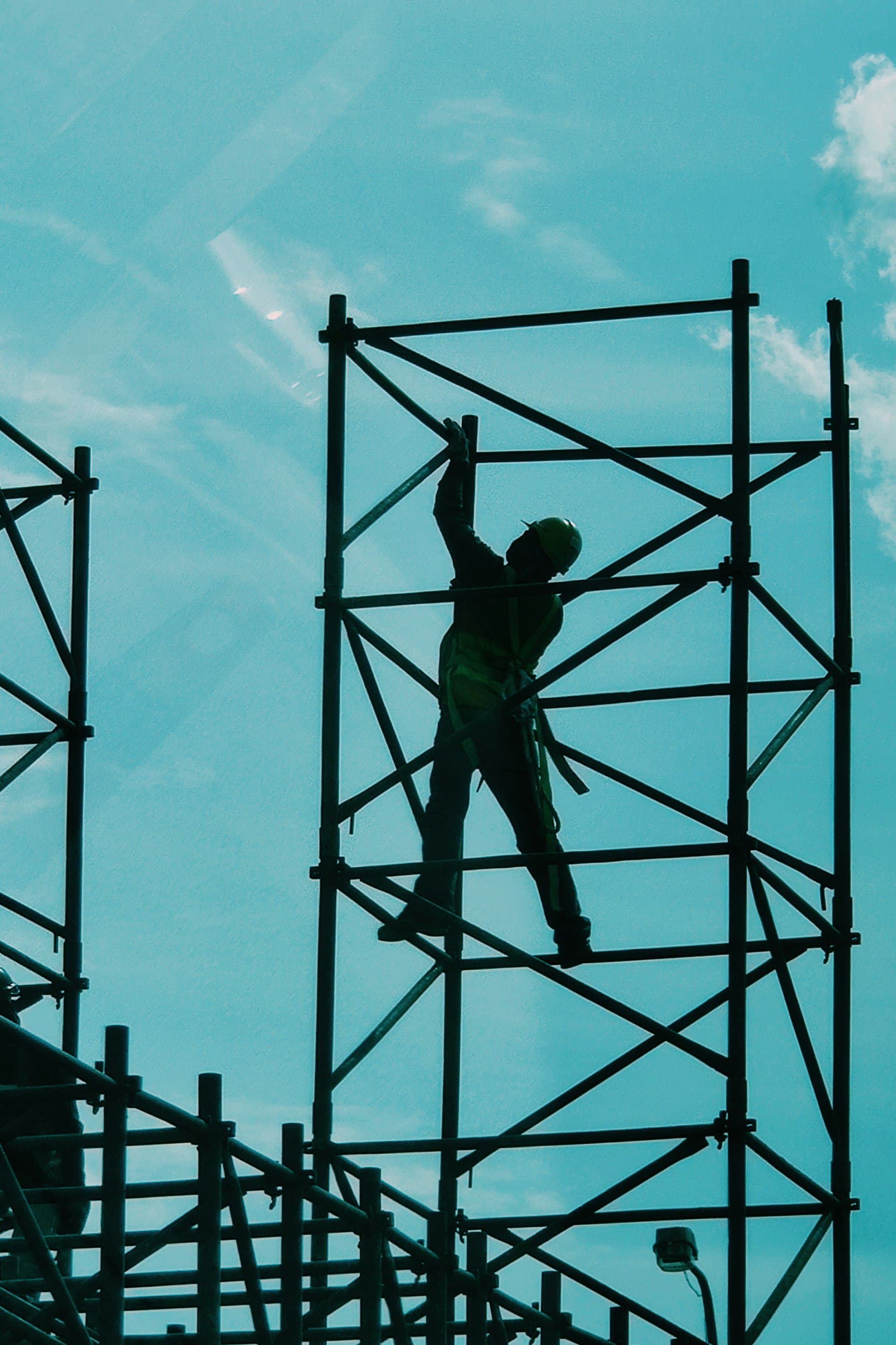 Silhouette of a scaffolder climbing a steel frame against a teal sky