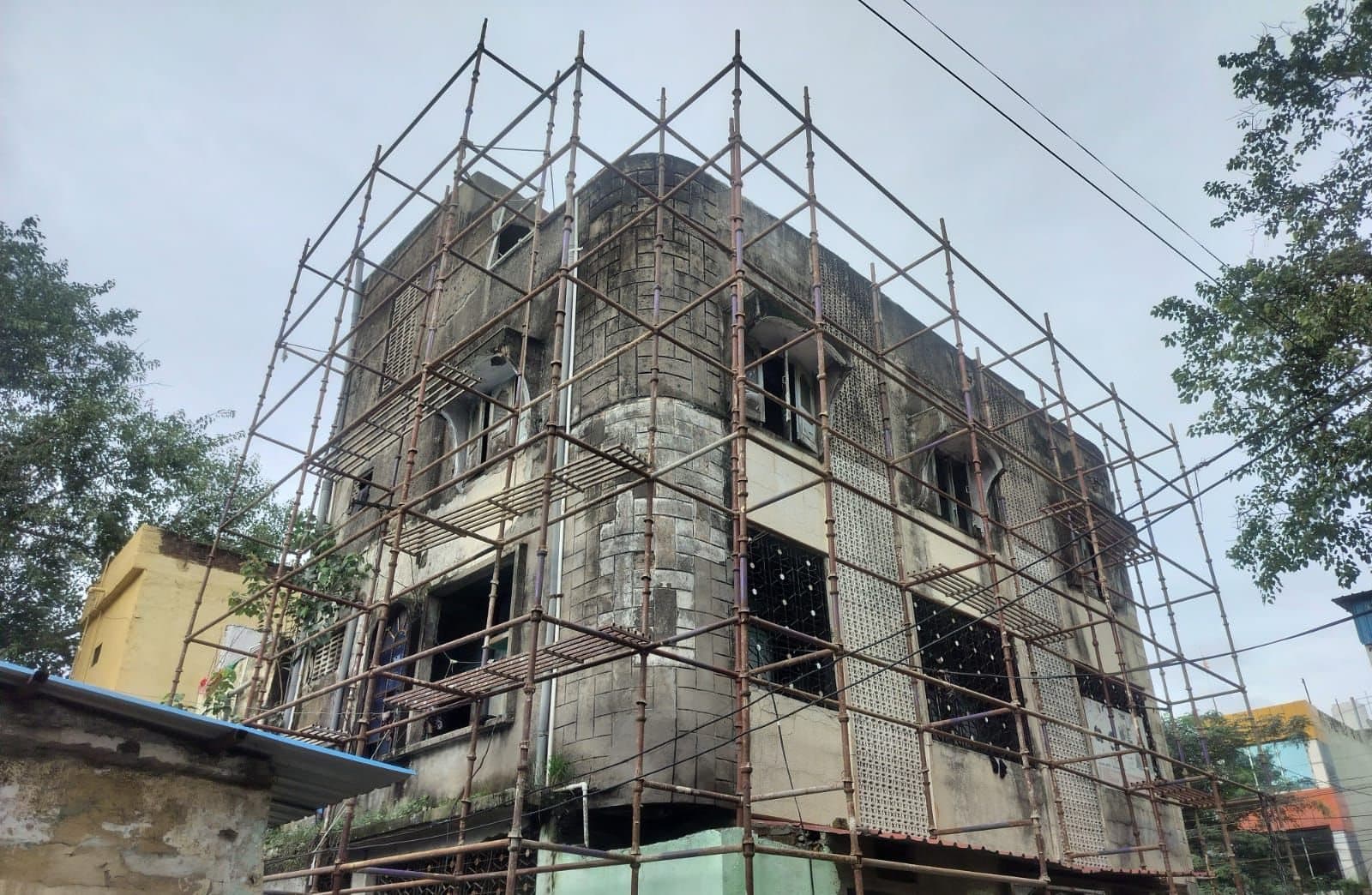 Scaffolding wrapped around the rounded corner of an old three-storey building under renovation in Indore