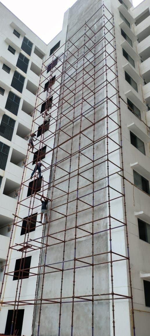 Scaffolders climbing a tall scaffold up the facade of a high-rise residential building
