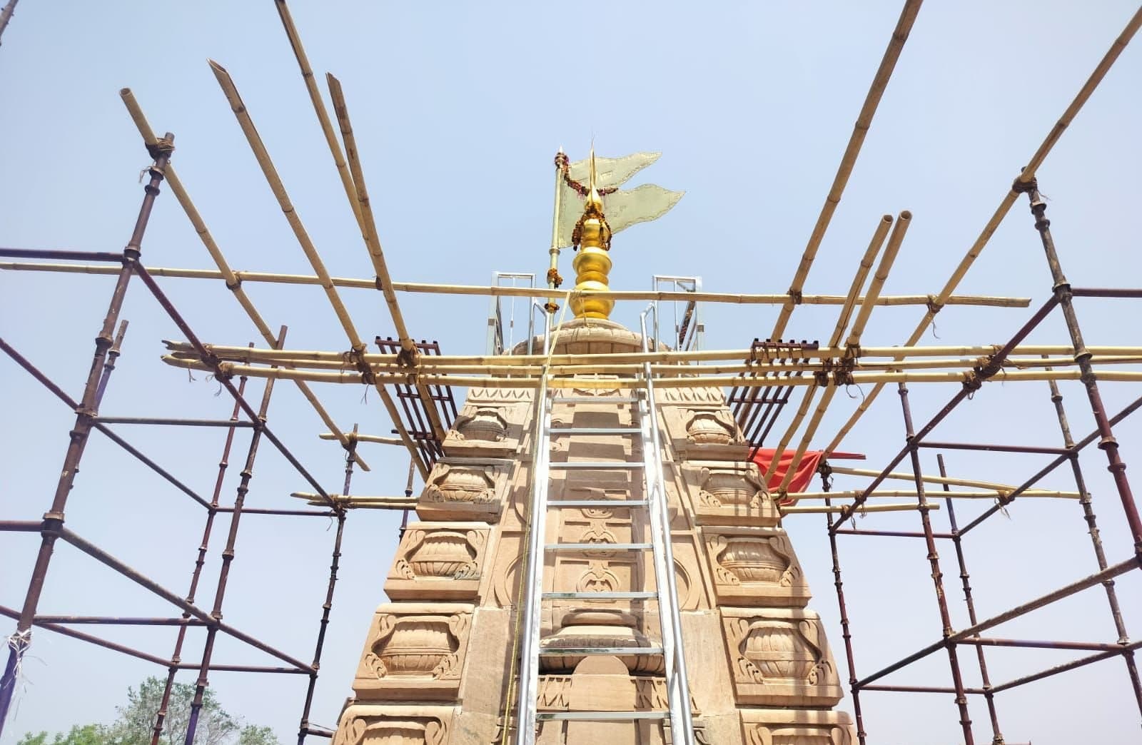Cup-lock and bamboo scaffolding around a carved sandstone temple shikhar with a ladder to the kalash