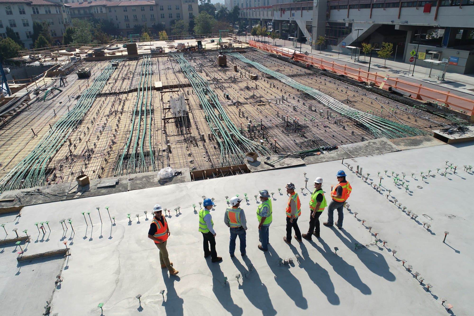 Site crew in hard hats and hi-vis vests reviewing a concrete deck from above