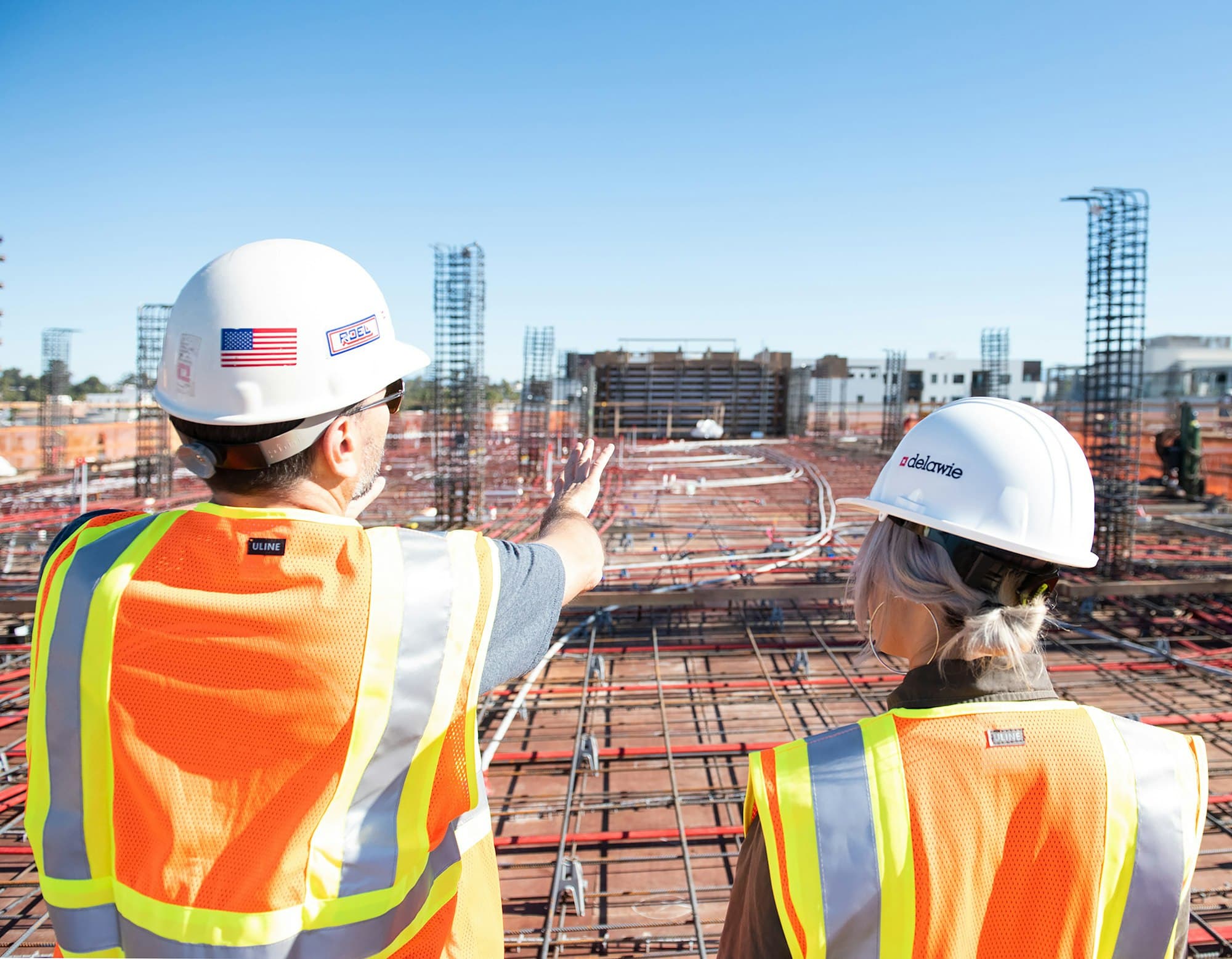 Two site supervisors in hard hats and safety vests looking across a construction site