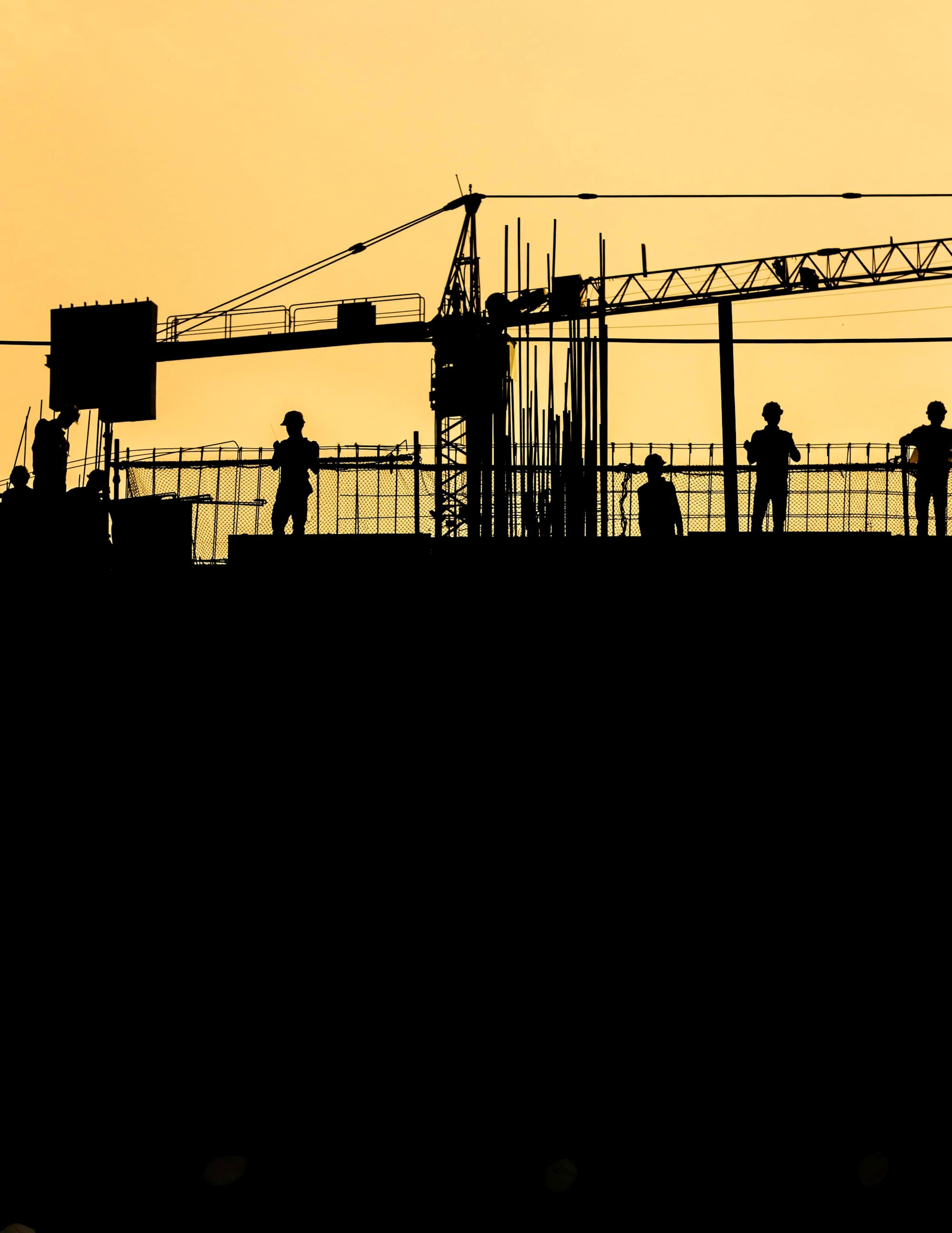 Silhouettes of construction workers and a tower crane at sunset