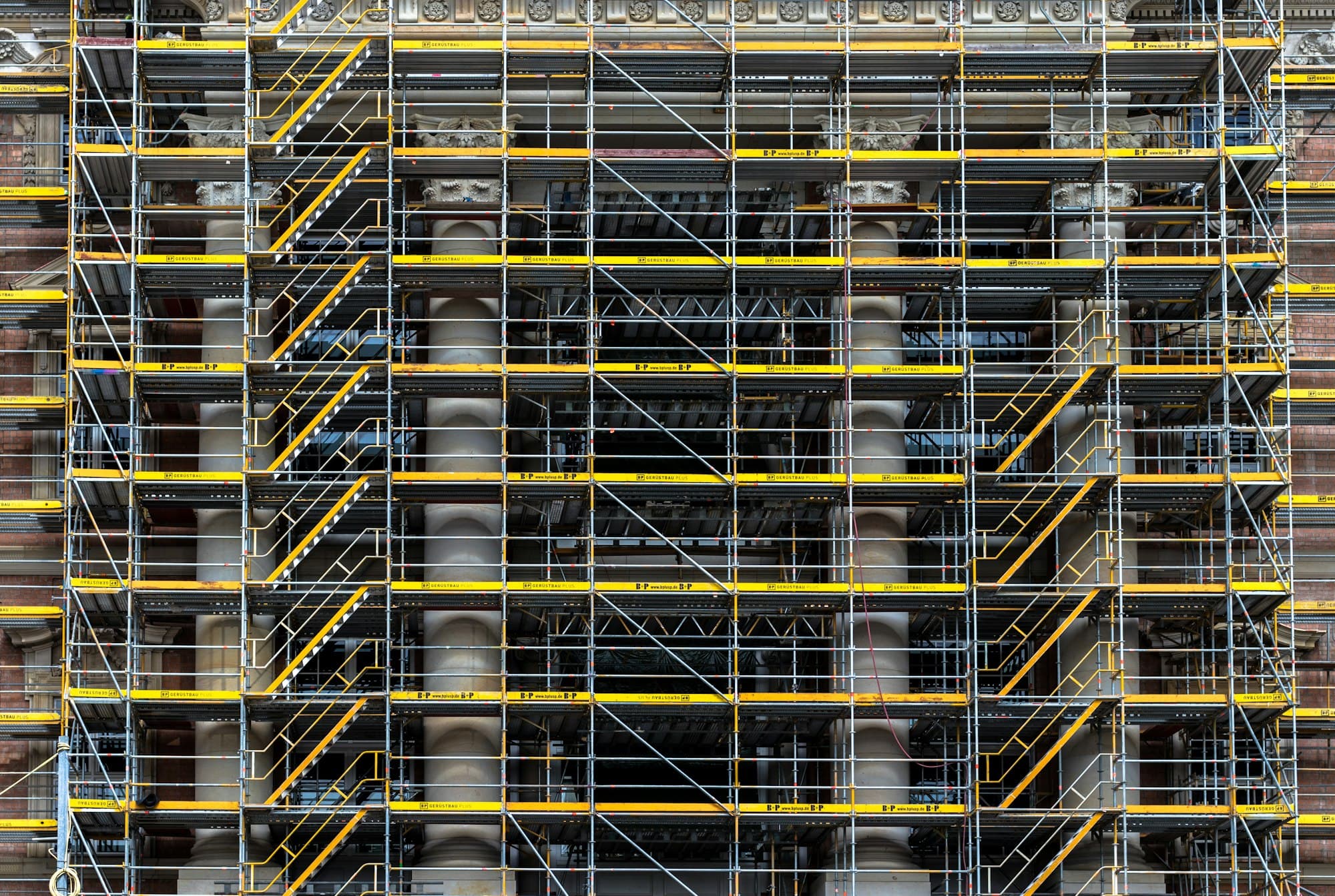 Facade covered in a dense grid of steel scaffolding with yellow toe boards