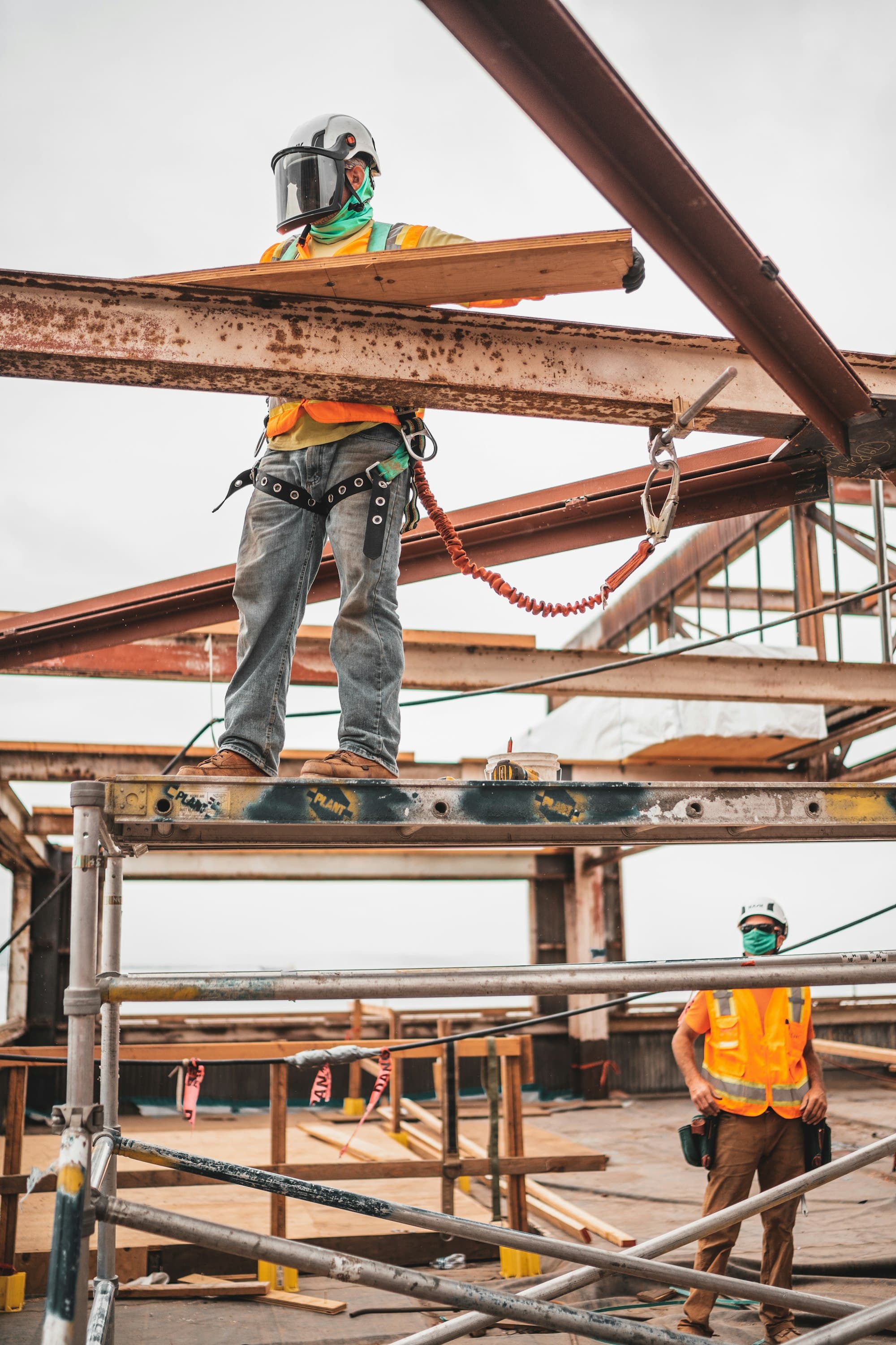 Worker on a scaffold handling timber boards between steel beams