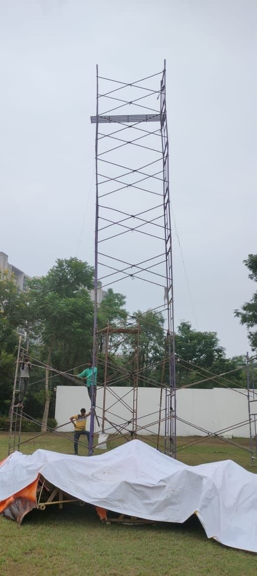 Tall frame scaffolding tower being erected by the crew on an open ground