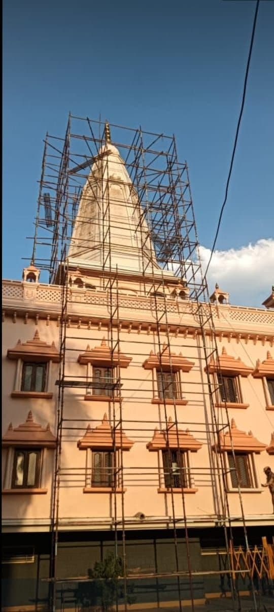 Tall scaffold erected around a white temple shikhar above a pink building
